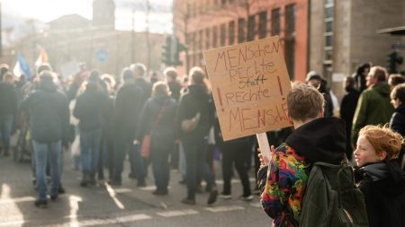 Menschen auf Demonstration mit einem Plakat im Fokus, welches den Titel Menschenrechte statt rechte Menschen trägt