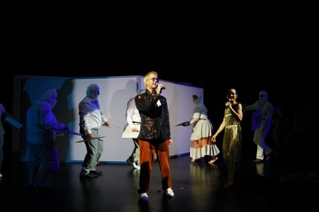 Auf der Bühne stehen zwei der Schauspieler:innen und singen ein Lied in glamourösen Kostümen. Im Hintergrund sind fünf der anderen Schauspieler:innen, verkleidet als Eisbären, zu sehen.